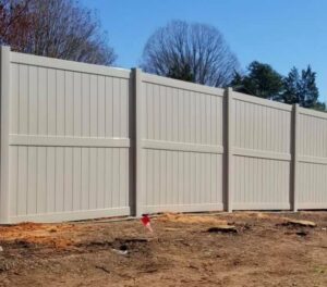 A beige vinyl fence installed on a dirt ground with trees in the background.