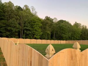 Wooden fence with pointed tops in front of a green forest.