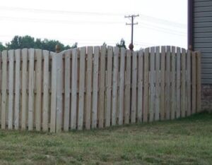 Tall wooden fence with a curved top design in a grassy area.