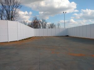 Empty outdoor sports court surrounded by white fencing under a cloudy sky.