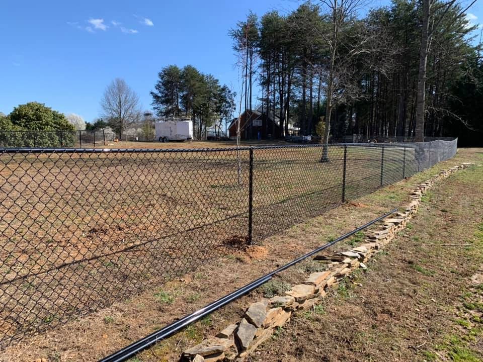 A fenced yard with a clear blue sky and some trees in the background.