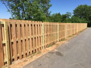 Long wooden fence along a paved path under clear blue sky.