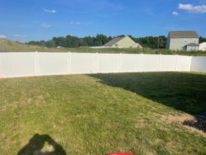 A sunny backyard with a white fence and green lawn.