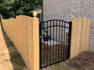 Black metal gate between wooden fence panels in a backyard.
