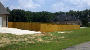 A wooden fence enclosing a backyard with houses and trees in the background.