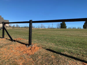 Newly installed black metal fence post in a grassy field under a clear blue sky.
