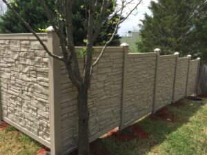 A stone-textured privacy fence next to a tree in a backyard.
