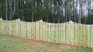 A wooden fence with a scalloped top in front of a forest.