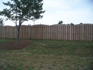 A wooden fence with a tree on a grassy lawn under a clear sky.
