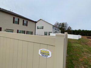 A beige fence with a security sign in front of residential buildings on a cloudy day.