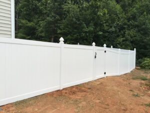 A tall white vinyl fence with a gate in a backyard area.