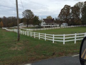 A white fence enclosing a grassy yard with houses in the background.