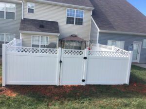 White vinyl fence with a small gate in a backyard.