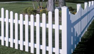 White picket fence in a green yard with trees.
