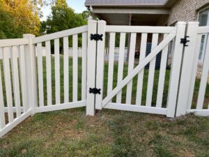 White wooden garden gate with black hinges in a backyard.