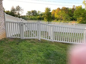 White wooden fence gate enclosing a grassy yard with a road beyond.