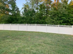 A white vinyl fence surrounds a grassy yard with trees in the background.